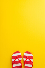 Celebrate the spirit of summer with this captivating top vertical view minimal flat lay. Featuring a pair of red striped flip-flops on a vibrant yellow backdrop, with an empty space for text or advert