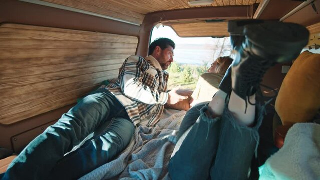 Cute happy young couple woman and a man lying talking feel happy in a car with a tent on the roof. Mini van. Camper vacation outdoors. Travel. Trip. Romantic. Vacation