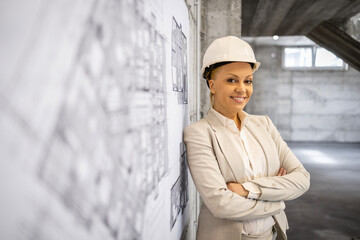 Portrait of beautiful woman engineer in business suit and safety helmet standing by the project blueprint at construction site.