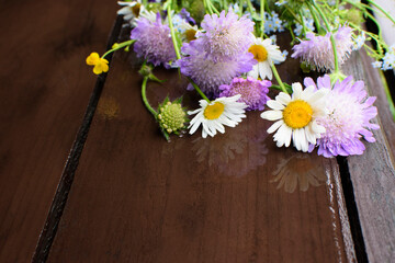 A romantic bouquet of wildflowers lying on the dark brown wooden table. Summertime. Copy space. Selective focus. 