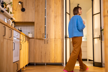 Kitchen interior with female person walking. Stylish interior of studio apartment made wooden materials. Domestic lifestyle