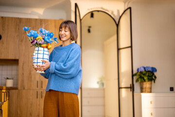 Young woman carries flowers in vase, decorating kitchen interior with fresh flowers or having some household chores - 608219188
