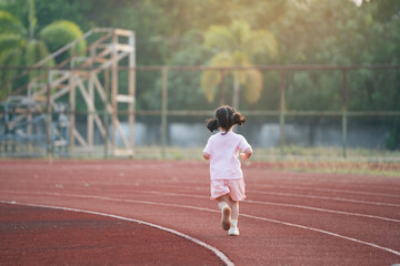 Back side. Baby asian girl run jogging at running track, field at stadium. little girl running...