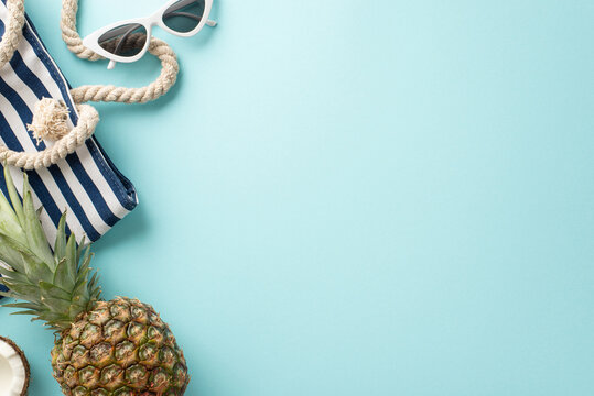 Immerse yourself in the essence of summer vacation with this captivating top-down view of sunglasses, fruit, bag, on a tranquil pastel blue surface. An empty space invites your text or advert