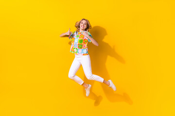 Fototapeta na wymiar Full length photo of cool cheerful woman dressed flower print t-shirt jumping high showing two thumbs up isolated yellow color background