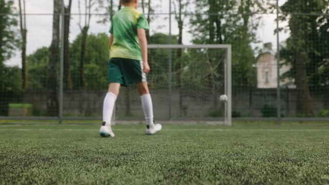 The boy dressed in football uniform is practicing on a mini football stadium. A close-up shot of the foot striking kicking the ball, resulting in a scored goal.
