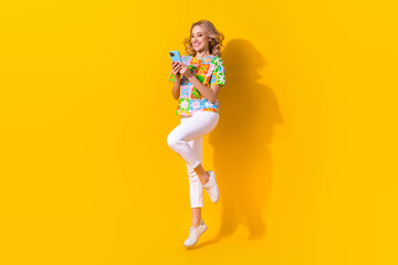 Fototapeta na wymiar Full length photo of cheerful sweet woman dressed t-shirt typing telegram facebook sms jumping isolated yellow color background