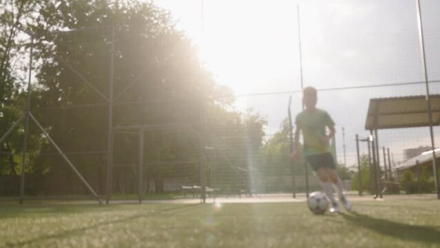 Blur shot. Boy dressed in football uniform is practicing on a mini football stadium. The young footballer skillfully dribbles the ball, using feints and moves forward.