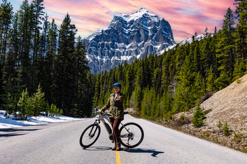 Woman cyclist on the track. Road to the mountains. Trail into the mountains and into the forest. Banff National Park.