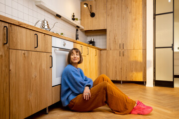 Young woman sitting on a kitchen floor at new and stylish studio apartment. Concept of new home interiors and leisure at home