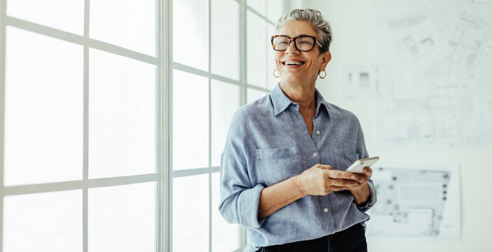 Mature business woman smiling and using a mobile phone in her office