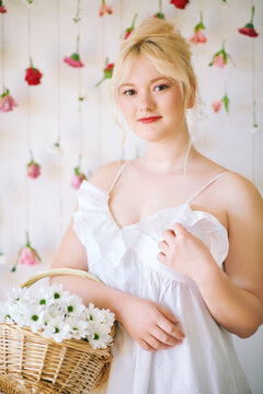 Studio portrait of pretty young teenage 15 - 16 year old girl wearing summer dress, posing on white background with hanging roses, holding basket with daisy flowers, beauty and fashion concept