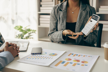 Fototapeta premium Asian businesswoman analyzes reports pointing to graphs, holding pens using laptops, business contacts, consulting to plan, financial statements, remote pictures.