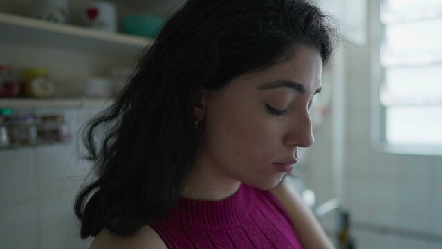 Contemplative young woman closeup profile face in deep thought. Pensive female person in 30s thinking about decision while standing at kitchen
