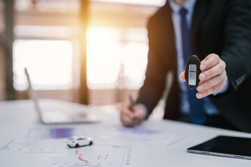 Close-up hand of car salesman handing over your new car keys at a desk with a laptop. dealership and online sales concept.