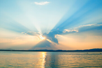 Sea landscape - sea water surface lit by sunset summer light. Sea summer nature with mountain range and colorful clouds