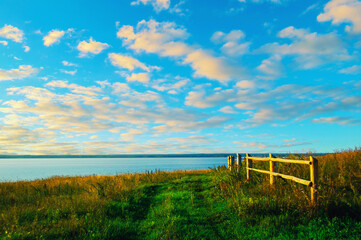 Fototapeta premium Summer landscape, field pathway along the lake, dramatic colorful sunset sky