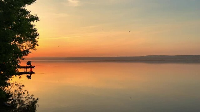Side view of a fisherman on the pond. Fishing at sunset. Russian fisherman with fishing rods on the background of a pond and a golden sunset. Russia, Votkinsk