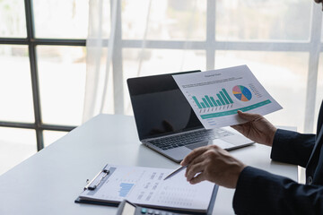 hand of business woman hold smartphone use analyzing and calculating the annual income and expenses, a financial chart and financial report, technology and bussiness concept.