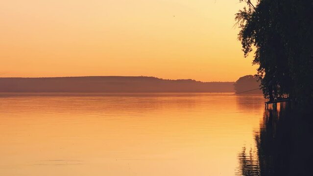 Side view of a fisherman on the pond. Fishing at sunset. Russian fisherman with fishing rods on the background of a pond and a golden sunset. Russia, Votkinsk