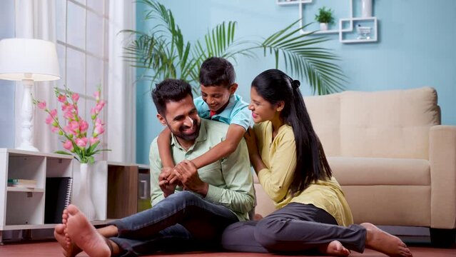 Happy Indian couple with son playing by cuddling on floor at home during weekend holidays - concept of family time, Joyful togetherness and Family bonding
