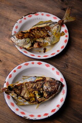 grilled pomfret on an old tin plate, on a brown wooden table. Ikan bawal bakar. sea food. fish barbecue. Mediterranean food. Indonesian food. 