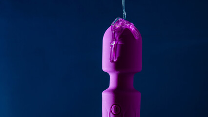 Intimate lubricant pours on a purple vibrator on a blue background. Copy space.  - obrazy, fototapety, plakaty