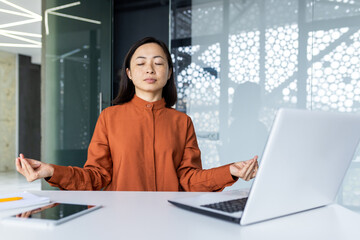 Young beautiful Asian web developer working inside office building, woman resting meditating at workplace with eyes closed, female worker using laptop to write code - obrazy, fototapety, plakaty
