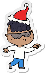 hand drawn sticker cartoon of a boy wearing sunglasses pointing wearing santa hat