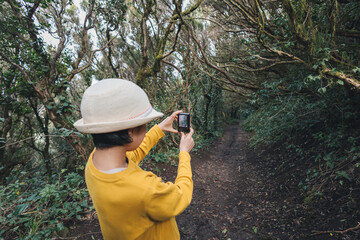 Teenage girl in yellow shirt and straw hat taking pictures of the Anaga forest in Tenerife
