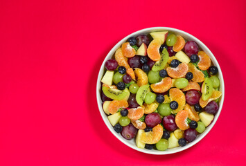 Healthy fresh fruit salad bowl on red background. Top view. Healthy food concept, healthy high vitamin fruit, mixed fruit background.