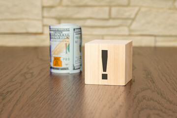 wooden cube with exclamation point and banknotes dollars on wooden table. concept of uncertainty, faq, questions and answers