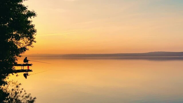 Side view of a fisherman on the pond. Fishing at sunset. Russian fisherman with fishing rods on the background of a pond and a golden sunset. Russia, Votkinsk