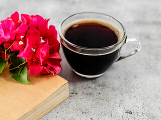 Close up shot of black coffee with beautiful pinks flowers placed on book.