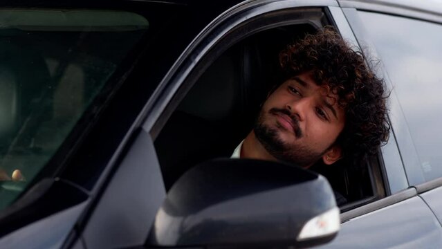 A young man with curly hair sticks his head out of the car window and sighs languidly. An Indian man in a business suit sits in a car and is indignant because of the traffic jam on the road.