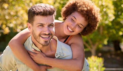 Portrait Of Loving Multi-Racial Couple With Man Giving Woman Piggyback Outdoors In Garden