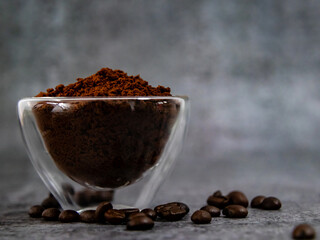 Coffee powder in glass bowl with beans scattered below.