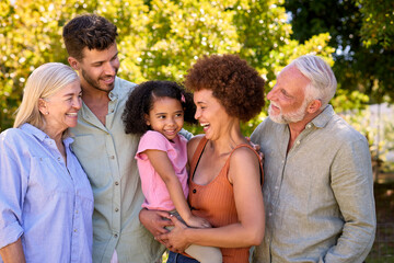 Portrait Of Multi-Generation Family Standing In Garden Smiling At Camera