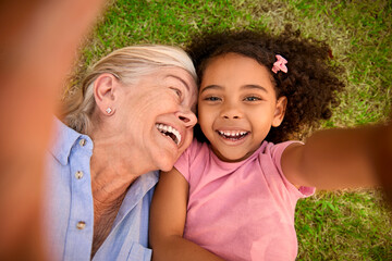 POV Overhead Shot Of Grandmother And Granddaughter Lying On Grass Taking Selfie On Mobile Phone