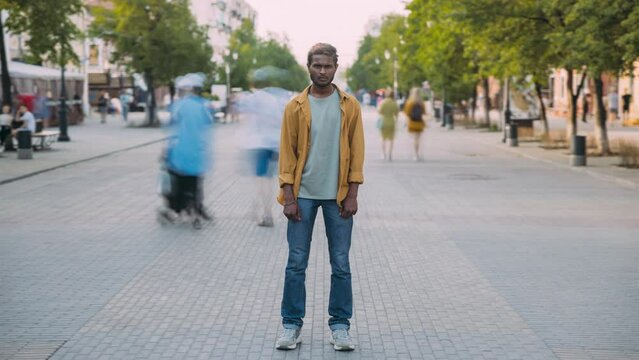 Time lapse portrait of serious Indian man standing in street alone while people moving around. Society and urban lifestyle concept.