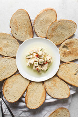 Top view of marinated feta cheese cubes on white plate surrounded by toasted slices of bread. Cheese cubes marinating in herb oil with bread, flat lay of feta cheese and bread on a white plate