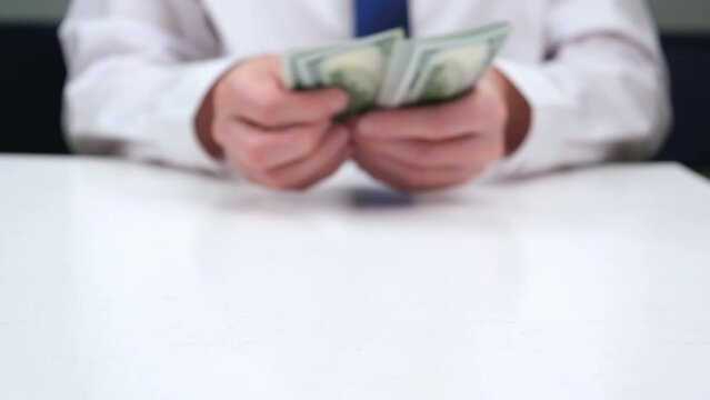 businessman in a blur counts the cash hundred-dollar bills of the USA at the table, gives them away. focus on money. close-up. the concept of venality, bribery, corruption. the hand that gives money.