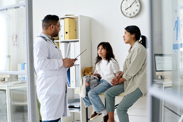 Mom and child talking to doctor while he writing prescription during their visit to hospital