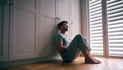 Depressed Man Suffering With Poor Mental Health Sitting On Floor At Home