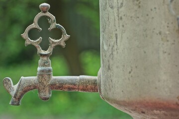 one very old iron tap from a very old classic retro traditional samovar for tea on a green background outdoors during the day