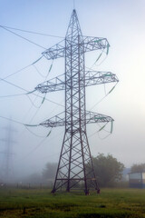 Electrical substation with transformers, equipment and high voltage pylons in the fog on an early summer morning.