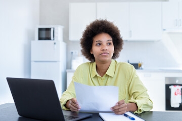 Stressed young black lady lost in heavy thoughts hold paper document deal with debt bankruptcy think of solving money problem. Worried mixed race woman concerned with bad news received by mail letter.