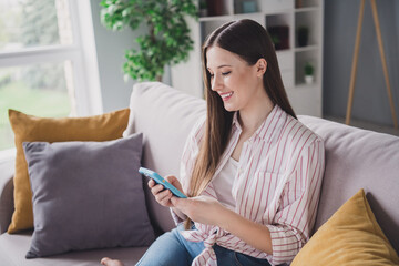 Photo of funny cute young lady dressed striped shirt sitting couch chatting instagram twitter...