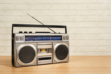 Old vintage portable radio receiver tape cassette recorder on wooden table in front of white brick...