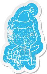 happy quirky cartoon distressed sticker of a pig with xmas present wearing santa hat